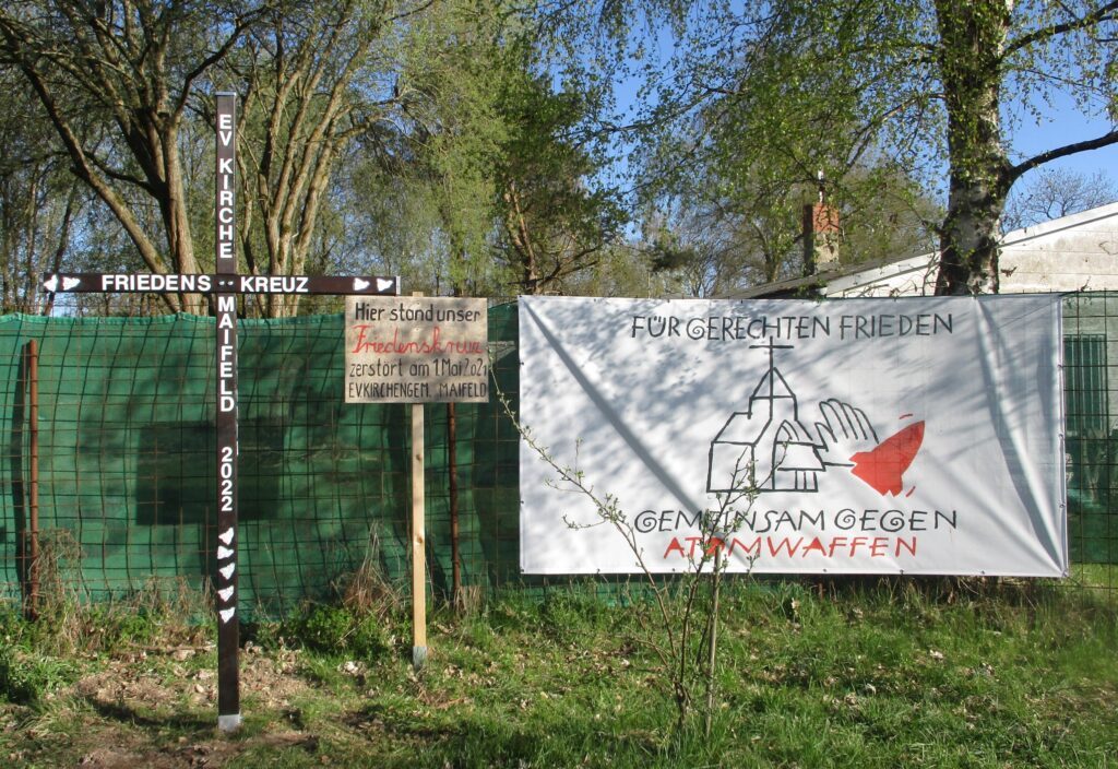 Zu sehen ist das Friedenskreuz unserer Kirchengemeinde sowei ein Transparent gegen  Atomwaffen. Das Kreuz steht auf der Friedenswiese vor dem Fliegerhorst in Büchel.